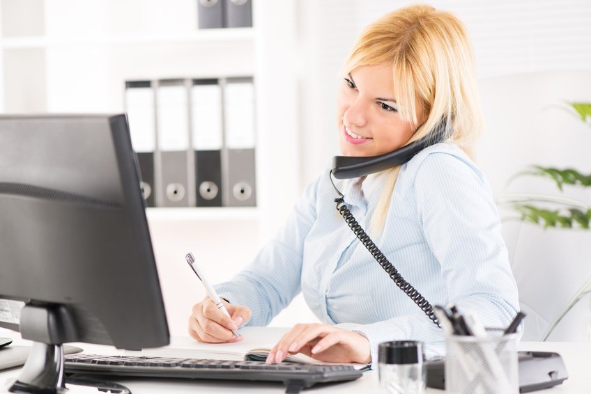 A woman sitting at a desk on the phone typing